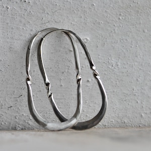 May include: A pair of silver hoop earrings. The earrings have a hammered texture and a twisted design at the top. The hoops are oval-shaped and have a simple, elegant style.