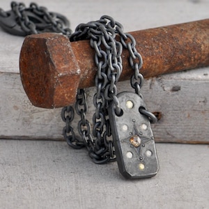 May include: A silver-toned metal pendant necklace with a rectangular pendant featuring a starburst design and a central amber-colored stone. The pendant is adorned with small, round, white and yellow accents. The necklace chain is a matching silver color.