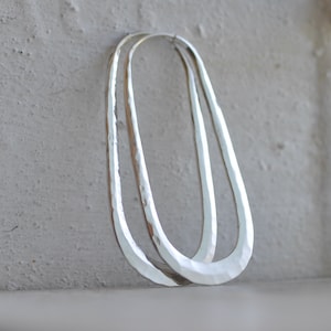 May include: A pair of silver hammered oval hoop earrings. The earrings are made of thick, textured metal and have a simple, modern design.
