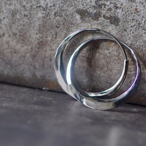 May include: Silver hoop earrings with a hammered finish. The earrings are thick and have a rounded shape.