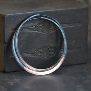 May include: A pair of hoop earrings with a silver and rose gold finish. The earrings are made of two bands of metal, one silver and one rose gold, that are joined together at the top.