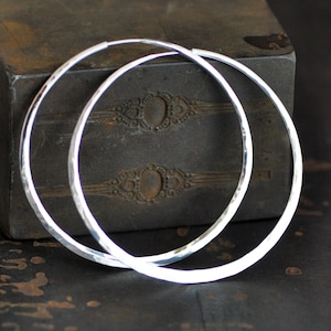 May include: A pair of large, silver hoop earrings with a hammered texture. The earrings are made of sterling silver and are approximately 2 inches in diameter.