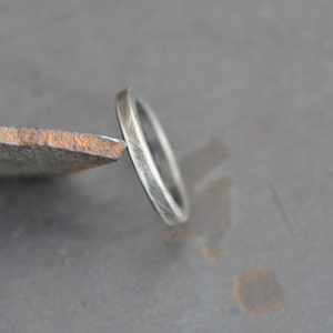 May include: A close-up of a silver ring with a textured surface. The ring is thin and appears to be made of metal. The ring is resting on a piece of metal with a rusty appearance.