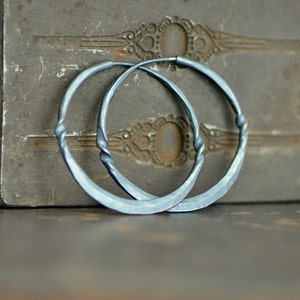 May include: A pair of silver hoop earrings with a hammered finish. The earrings are large and have a slightly curved shape.