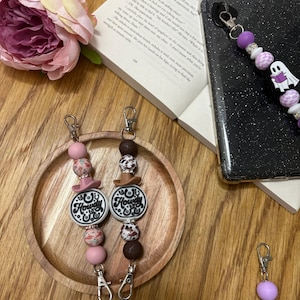 May include: Two pink and brown beaded keychains with a cowgirl theme. The charms on the keychains say "Howdy" in black lettering.