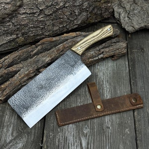 以下が含まれることがあります： 木製のハンドルと革製の鞘が付いた、手打ちの大型の肉切り包丁。肉切り包丁はハンマー仕上げで、わずかに湾曲した刃をしています。