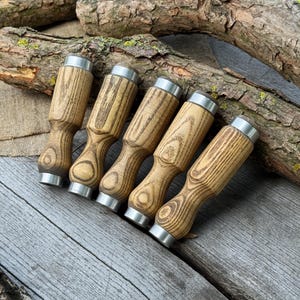 May include: Five wooden chisels with silver metal accents. The chisels have a light brown wood grain pattern and are arranged on a weathered wooden surface. The handles are a light brown color with a unique shape.