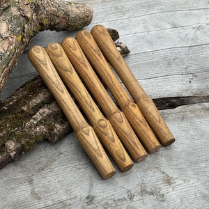 May include: Six wooden stir sticks with rounded handles and a light brown finish, arranged diagonally. The sticks are displayed on a weathered wooden surface, highlighting the natural wood grain. Each stick is approximately 15 cm long.