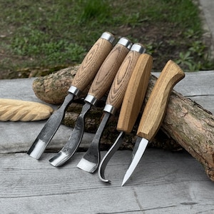 May include: A set of five wood carving tools with wooden handles and metal blades. The handles are light brown with a silver metal band. The blades have different shapes, including a straight blade, curved blade, and a pointed knife.