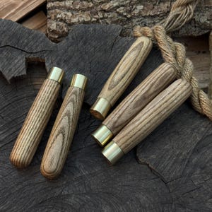 Puede incluir: Varios mangos de madera con férulas de latón. Los mangos presentan un patrón de vetas de madera natural y tienen forma cilíndrica. Las férulas de latón añaden un toque de elegancia. Dispuestos sobre una superficie de madera oscura.