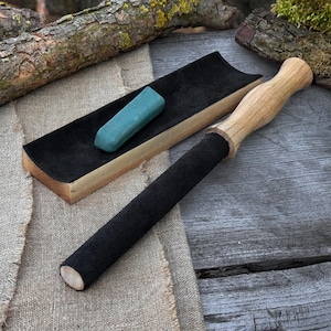 Peut inclure: Un bâton de billard avec une poignée noire et un manche en bois clair. Un plateau doublé de feutre noir contient un cube de craie turquoise. L'ensemble est présenté sur une surface en bois rustique, évoquant le thème du billard.