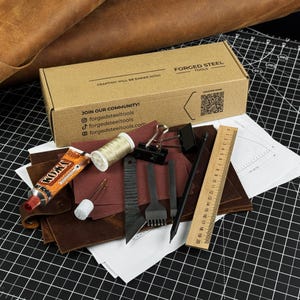 Puede incluir: Un kit de artesanía en cuero con herramientas y materiales. El kit incluye una caja de cartón con el texto "FORGED STEEL TOOLS" y "CRAFTING WILL BE EASIER NOW". Hay un tubo de pegamento KOMA, hilo, agujas, una regla (aproximadamente 20 cm) y varias herramientas de trabajo del cuero.