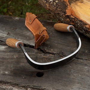 May include: A curved draw knife with wooden handles and a leather sheath. The blade is made of steel and has a sharp edge. The handles are made of wood and are attached to the blade with metal rings. The sheath is brown and protects the blade.