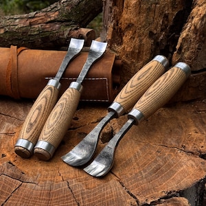 May include: Four wood carving gouges with light-colored wood handles and silver metal ferrules. The steel blades feature a curved, spoon-like shape with a textured, dark finish. Two tools are positioned horizontally, while two are angled.