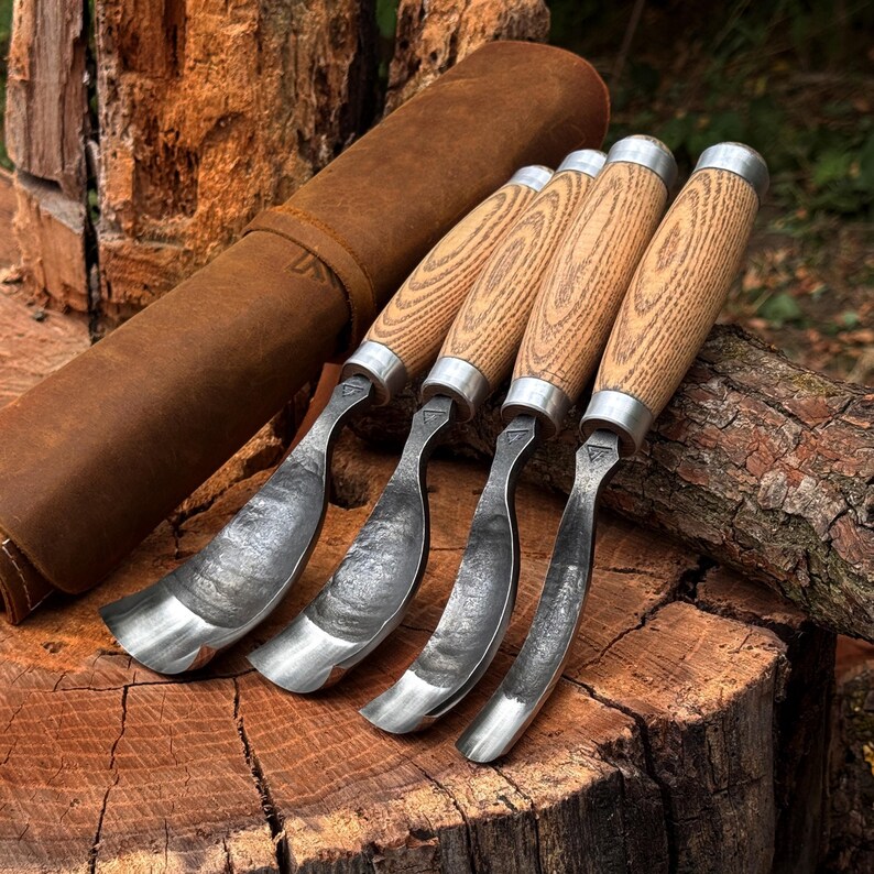 Pu&ograve; includere: Un set di quattro sgorbie curve per intaglio con lame in metallo testurizzato e manici in legno chiaro, accompagnate da una custodia arrotolabile in pelle marrone. Ogni utensile presenta una ghiera in metallo che unisce la lama al manico.