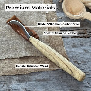 May include: A wood carving knife with a curved blade, protected by a brown leather sheath. The handle is made of solid ash wood. The blade is 52100 high-carbon steel. The text "Premium Materials" is at the top of the image.