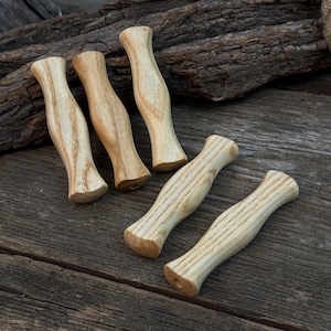 Peut inclure: Quatre poignées en bois clair avec un design incurvé. Les poignées sont faites d'un bois clair avec des motifs de grain visibles. Elles sont disposées sur une surface en bois vieilli, suggérant une esthétique rustique ou artisanale.