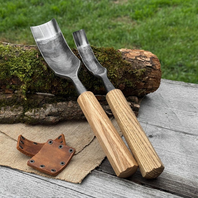 May include: Two wood carving gouges with curved steel blades and light-colored wooden handles. A small, brown leather sheath with metal eyelets rests on a burlap cloth. The tools are displayed on a weathered wooden surface.