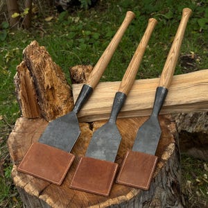 Timber slick chisels resting on a stump with leather sheaths, woodworking tools for outdoor carpentry