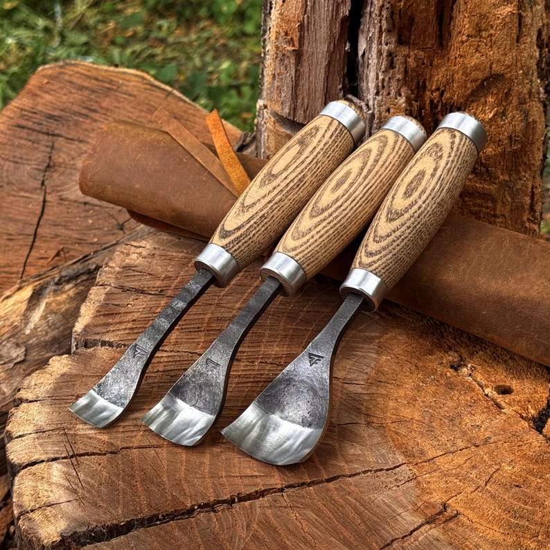 May include: Three hook knives with curved, dark forged steel blades and light-colored wood handles featuring prominent grain patterns. Each tool has a silver-toned metal ferrule connecting the blade to the handle and a small stamped logo.