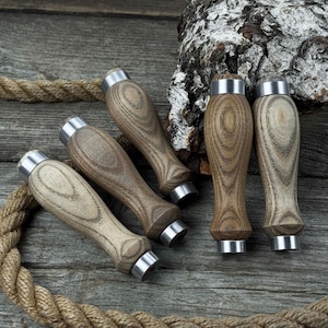 May include: A collection of wooden handles with a silver metal band at the top and bottom. The handles are various shades of brown and tan, with a wood grain pattern. They are arranged on a weathered wooden surface with a rope.