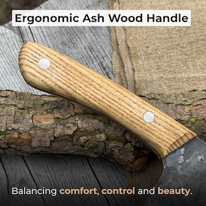 Puede incluir: Primer plano de un mango de cuchillo de madera de fresno. El mango es de color marr&oacute;n claro con un patr&oacute;n de vetas de madera y dos remaches plateados. El texto "Ergonomic Ash Wood Handle" est&aacute; en la parte superior y "Balancing comfort, control and beauty" en la inferior.