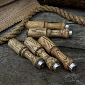 Könnte beinhalten: Eine Sammlung von Holz-Flaschenverschlüssen mit hellbraunem Finish und silberfarbenen Metallakzenten. Die Verschlüsse sind auf einer verwitterten Holzoberfläche angeordnet, mit einem Seil und einer Holzplanke im Hintergrund.