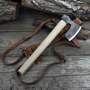Timmermansbijl. Scherp mes van koolstofstaal, essenhouten handvat, leren schede. Houtbewerkingsbijl. Gesmede bijl voor kamperen, bushcraft en wandelingen.