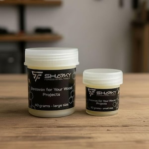 Puede incluir: Dos botes de cera de abejas Sharky para proyectos de madera. El bote más grande contiene 40 gramos, y el más pequeño 10 gramos. Ambos botes tienen tapas blancas y etiquetas negras con el logotipo de Sharky.