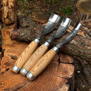 Puede incluir: Tres gubias para tallar madera con hojas met&aacute;licas curvas y mangos de madera de color marr&oacute;n claro. Cada herramienta cuenta con una virola de metal plateado que une la hoja al mango y un peque&ntilde;o logotipo grabado en el v&aacute;stago met&aacute;lico.