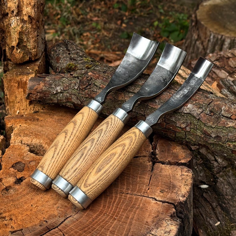 Puede incluir: Tres gubias para tallar madera con hojas met&aacute;licas curvas y mangos de madera de color marr&oacute;n claro. Cada herramienta cuenta con una virola de metal plateado que une la hoja al mango y un peque&ntilde;o logotipo grabado en el v&aacute;stago met&aacute;lico.