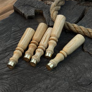 May include: A collection of five wooden stamp handles with brass accents. The handles are light-colored wood with a turned design, and the brass accents are at the base. The items are arranged on a dark, textured wooden surface.