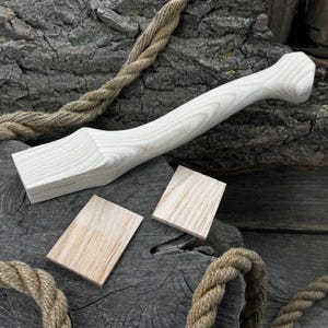 May include: A white wood axe handle with a natural wood grain. The handle is shown with two small pieces of wood that are likely for attaching the axe head.
