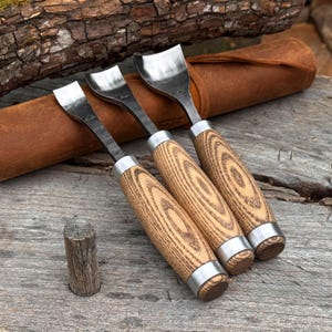 May include: Three metal wood carving gouges with curved steel blades and light brown wooden handles featuring a distinct grain pattern. Each tool has a silver metal ferrule at the top and bottom of the handle, and they are arranged in a row.