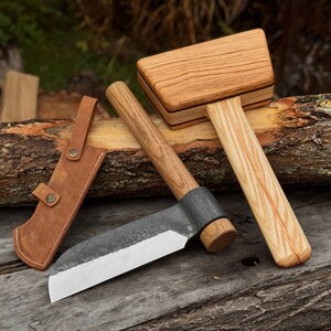 May include: A set of woodworking tools, including a wooden mallet, a hatchet with a leather sheath, and a small axe. The tools are made of wood and metal, with a natural finish. The hatchet has a curved blade.