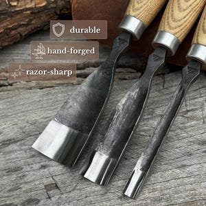 May include: Three wood carving chisels with light-coloured wooden handles and silver metal ferrules. The blades feature a dark, textured, hand-forged finish with polished, razor-sharp edges. Text overlays on the image read durable, hand-forged, and razor-sharp.