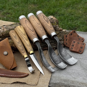 May include: A set of wood carving tools with wooden handles and metal blades. The tools are arranged on a wooden surface with a leather sheath and protective covers. The handles have a natural wood grain pattern.