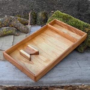 May include: A wooden tabletop game with a rectangular playing surface and a raised edge. The game has a small wooden piece in the center and a compartment on one side. The wood has a natural finish.