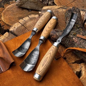 Puede incluir: Tres gubias para madera con hojas met&aacute;licas curvas y mangos de madera clara. Cada herramienta cuenta con una virola de metal que conecta el mango con la hoja de acero, la cual presenta un acabado oscuro y texturizado con un peque&ntilde;o logotipo.