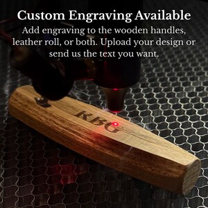 May include: A laser engraving machine marks the letters KBG onto a light brown wooden handle. The text Custom Engraving Available, Add engraving to the wooden handles, leather roll, or both. Upload your design or send us the text you want is visible.