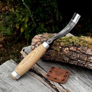 May include: A hook knife with a curved steel blade and a light-coloured wooden handle. The tool features a metal ferrule connecting the blade to the handle. A small, square brown leather sheath with metal rivets and a stamped logo sits nearby.