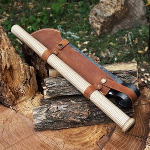 May include: A wooden-handled hatchet with a brown leather sheath and straps. The hatchet has a light-colored wooden handle and a dark metal blade. The sheath is a medium brown color and is secured with metal rivets.
