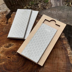 May include: A set of sharpening stones with a honeycomb pattern and the numbers 240# and 600# printed on them. The stones are gray and set in a wooden holder.