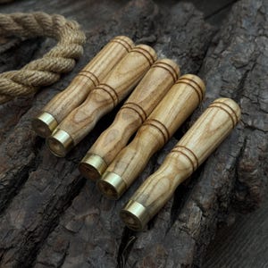 Może przedstawiać: Kolekcja sześciu drewnianych uchwytów z mosiężnymi tulejami. Uchwyty są jasnobrązowe z naturalnym wzorem słojów drewna. Mosiężne tuleje dodają blasku. Ułożone na ciemnej, teksturowanej powierzchni.