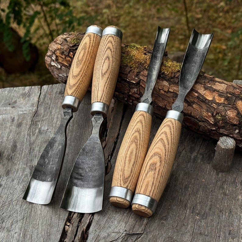 Puede incluir: Cuatro gubias para madera con mangos de madera clara y virolas de metal plateado. Dos herramientas presentan hojas de metal anchas y curvas, mientras que las otras dos tienen hojas en forma de U profunda. Cada hoja met&aacute;lica tiene un acabado oscuro y texturizado.