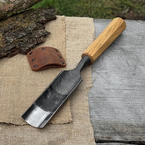Peut inclure: Un ciseau à gouge incurvé forgé à la main, avec un manche en bois clair et une lame en métal foncé. Un petit protège-outil en cuir marron avec des rivets est à côté du ciseau. Les outils sont sur une toile de jute et une surface en bois vieilli.