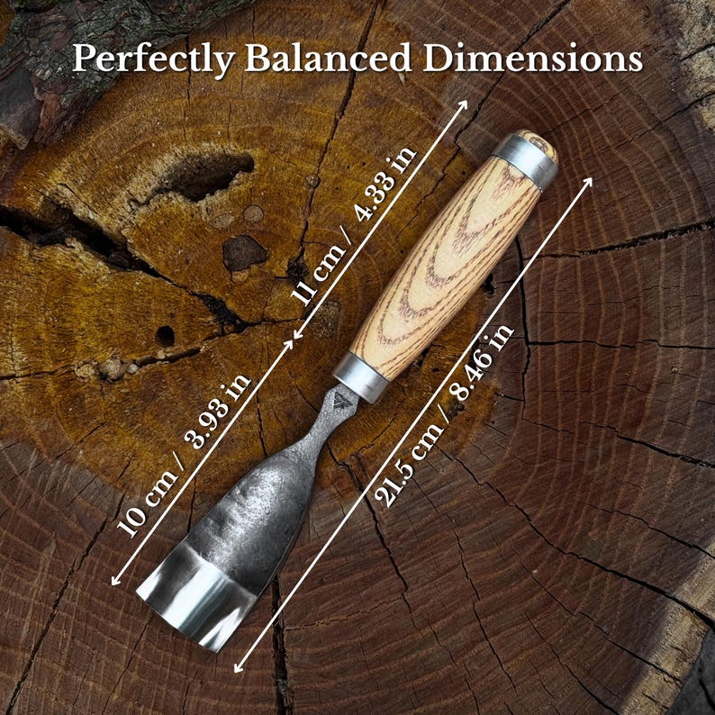 Pu&ograve; includere: Uno scalpello per legno in metallo con manico in legno chiaro e ghiera in metallo argentato. L'utensile presenta una lama curva ed &egrave; etichettato con le dimensioni 10 cm / 3,93 in, 11 cm / 4,33 in e 21,5 cm / 8,46 in. Il testo recita Perfectly Balanced Dimensions.