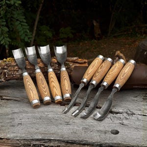 May include: A set of eight woodworking gouges featuring curved metal blades with a dark, textured finish and light brown wooden handles with visible grain patterns. Four gouges are positioned upright, while four are laid horizontally.