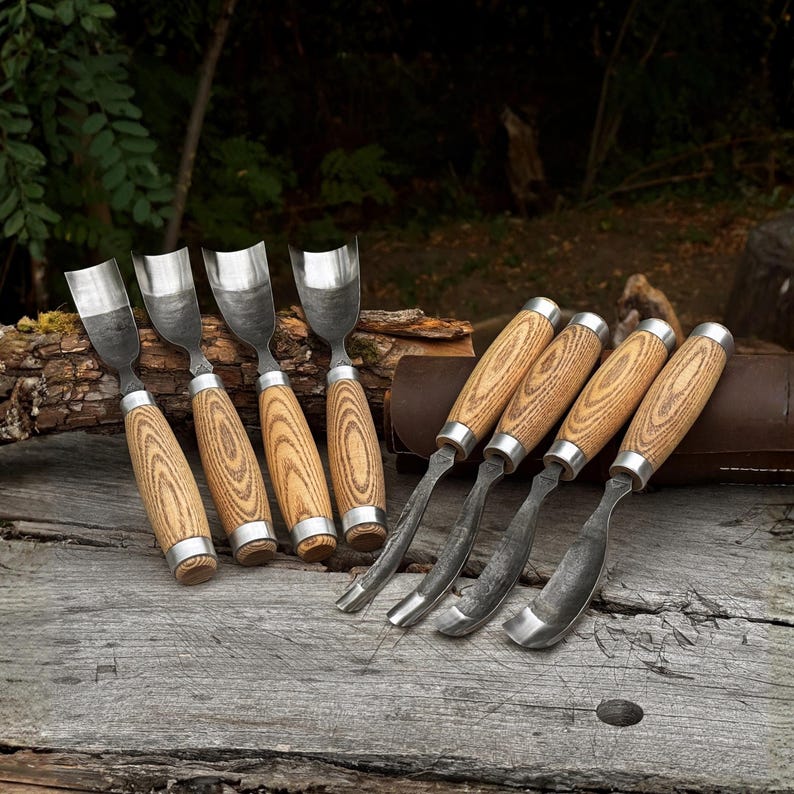 May include: A set of eight woodworking gouges featuring curved metal blades with a dark, textured finish and light brown wooden handles with visible grain patterns. Four gouges are positioned upright, while four are laid horizontally.