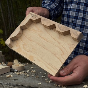 Könnte beinhalten: Ein helles Holzwerkzeug mit einem einzigartigen Stufenkantendesign. Das Werkzeug trägt die Aufschrift "FORGED STEEL - TOOLS" in der oberen linken Ecke. Das Werkzeug wird von einer Person gehalten, die ein blau-schwarz kariertes Hemd trägt.